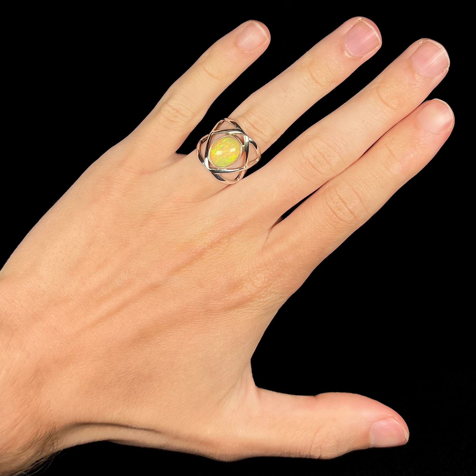 A silver Ethiopian opal ring with an open design worn on a hand against a black background.
