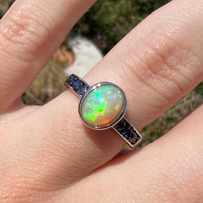 Front macro view of an Ethiopian opal ring worn on a finger in the sunlight, the opal's green colors showing.