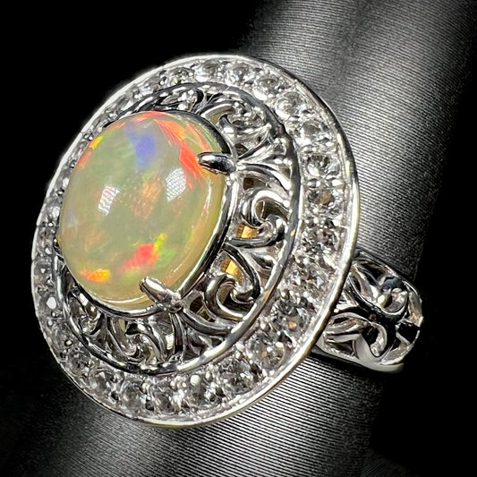Silver Ethiopian opal ring with a double halo of filigree and white topaz stones, shown at an angle.
