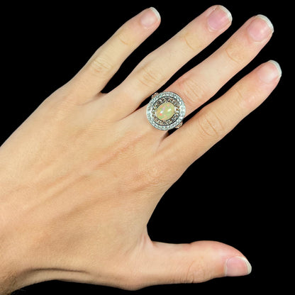 A silver Ethioipian opal statement ring with double halo worn on a hand against black background.