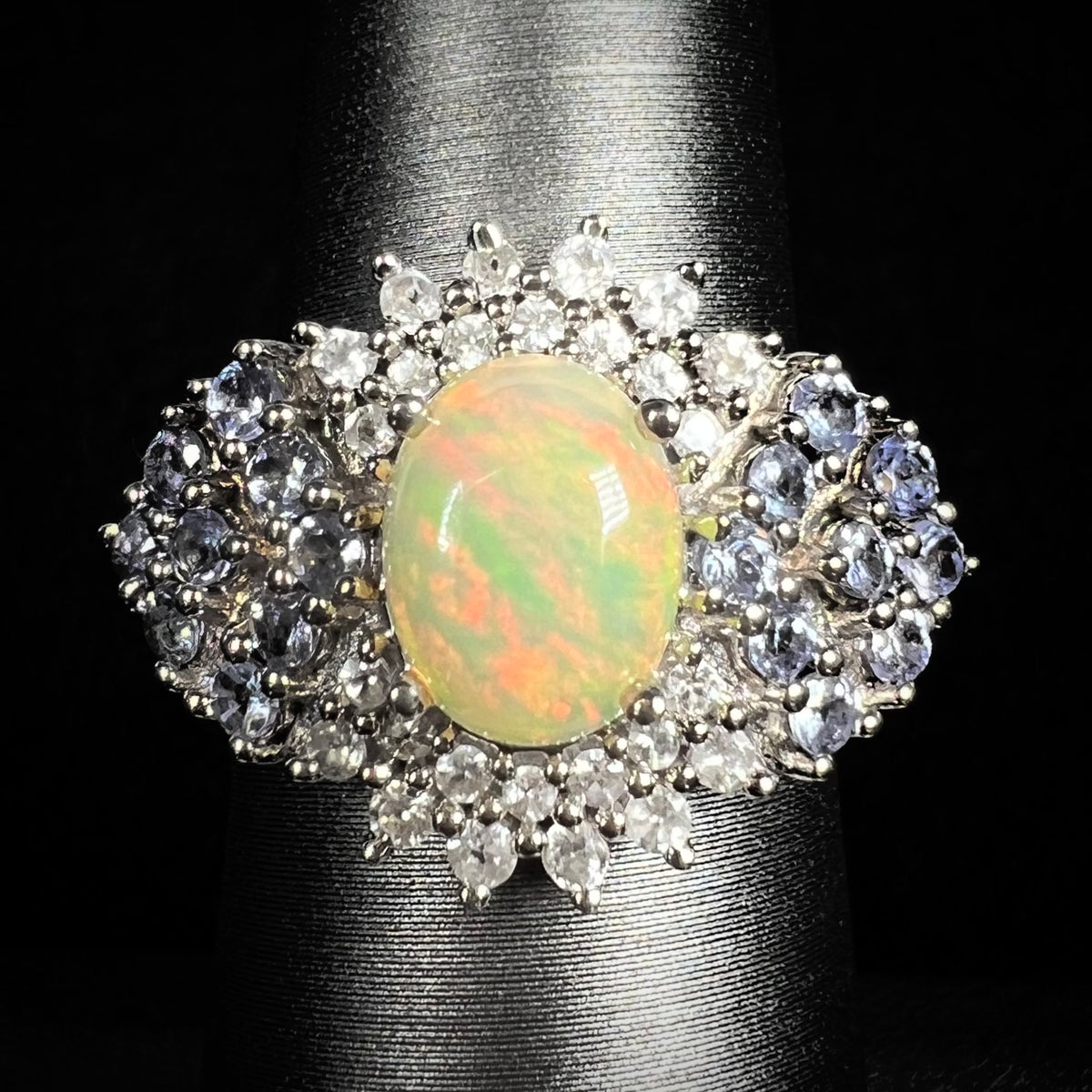 Close-up of women's sterling silver Ethiopian opal ring with clustered spray of tanzanite and white topaz accents, on ring display