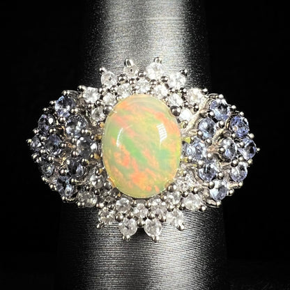 Close-up of women's sterling silver Ethiopian opal ring with clustered spray of tanzanite and white topaz accents, on ring display
