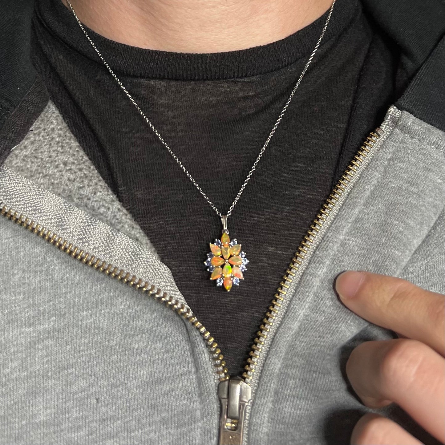 An Ethiopian opal and tanzanite cluster necklace, worn around a model's neck against a dark shirt under a hoodie.