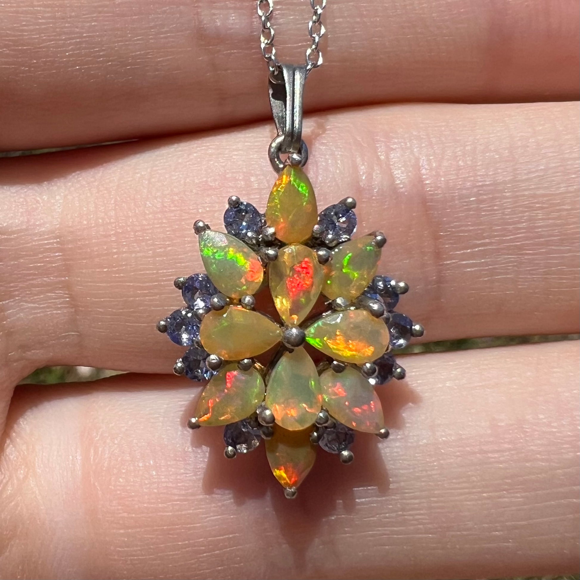 Close-up front view of an Ethiopian opal and tanzanite cluster necklace, held in the sunlight.