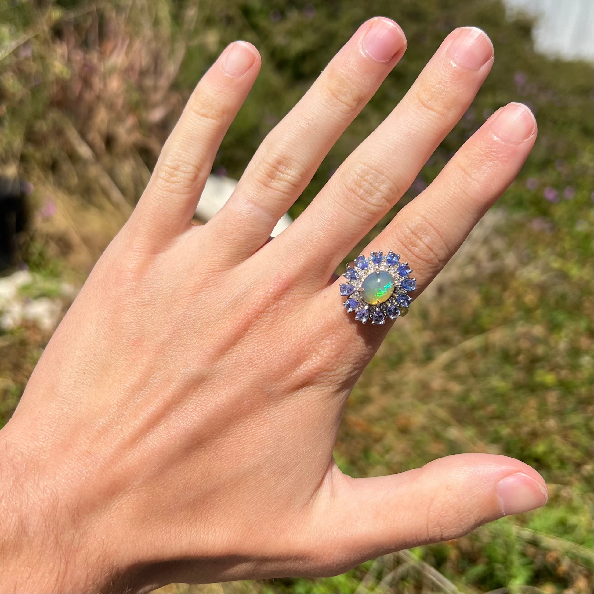 An Ethiopian opal and tanzanite starburst ring, worn on a hand at a distance in the sunlight.