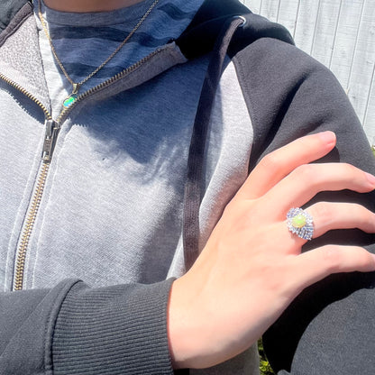 Close-up of person resting hand on opposing shoulder wearing Ethiopian opal and tanzanite ring in sunlight