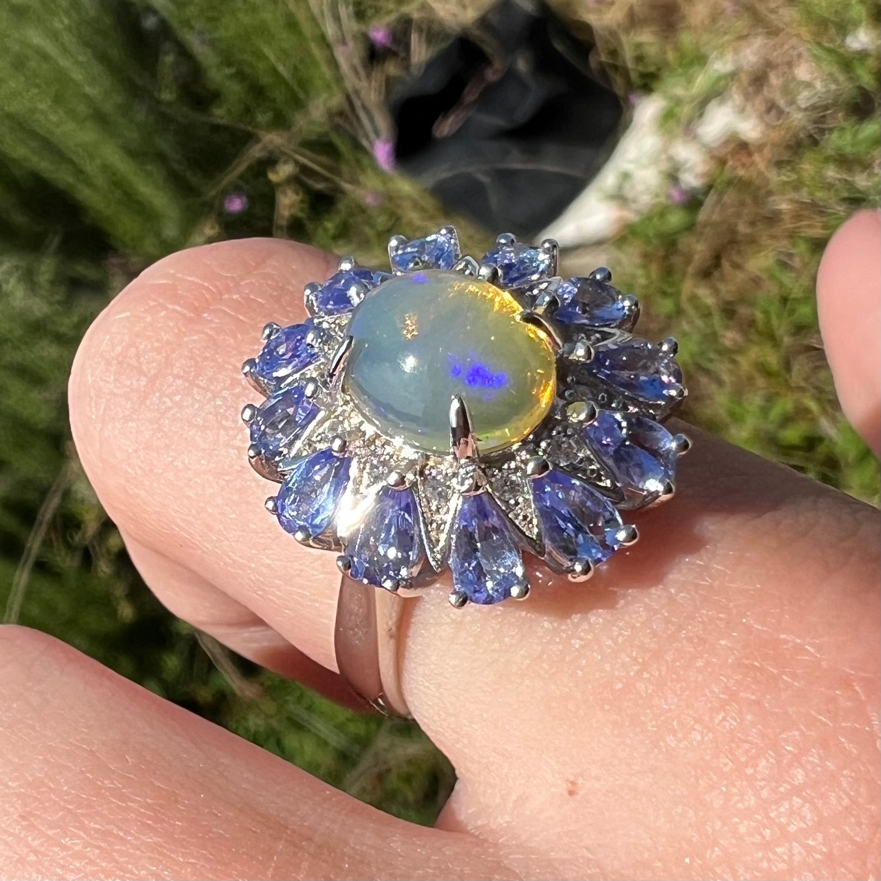 An Ethiopian opal and tanzanite ring shown in sunlight at an angle, worn on a finger.