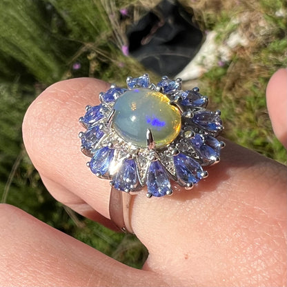 An Ethiopian opal and tanzanite ring shown in sunlight at an angle, worn on a finger.