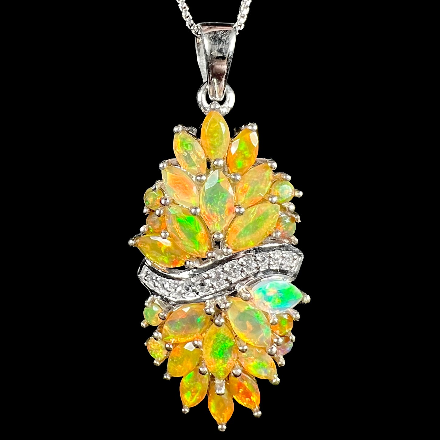 Close-up macro view of a faceted Ethiopian fire opal cluster necklace with a wavy row of white zircon accents, shown on a box chain against a black background.