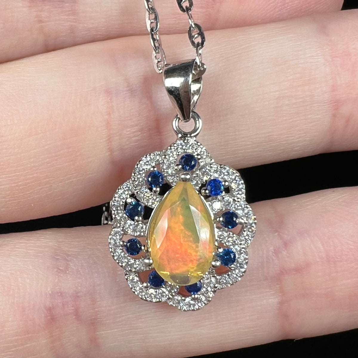 Close-up of faceted pear shaped Ethiopian opal and blue sapphire pendant, held in hand