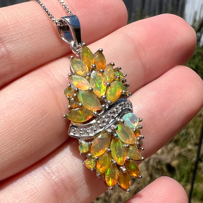 A faceted Ethiopian fire opal pendant made from sterling silver on chain shown from angled macro view in natural light, held in a hand.