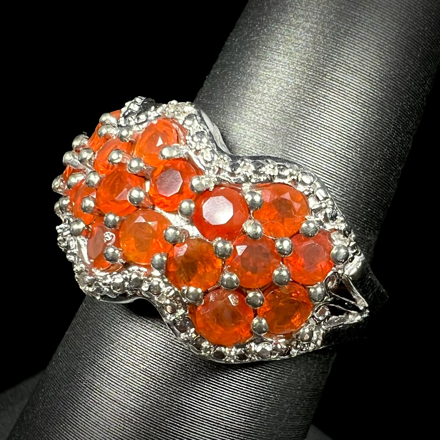 Angled close-up of a faceted round fire opal cluster ring in sterling silver, shown on ring display.