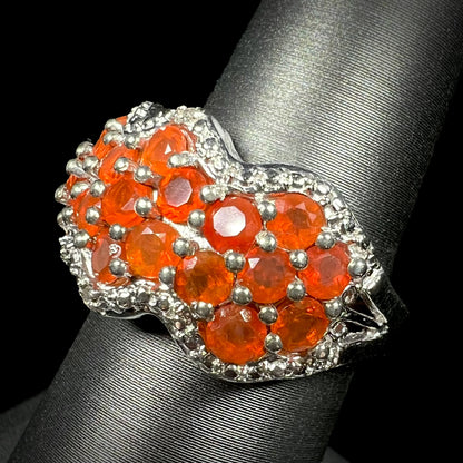 Angled close-up of a faceted round fire opal cluster ring in sterling silver, shown on ring display.