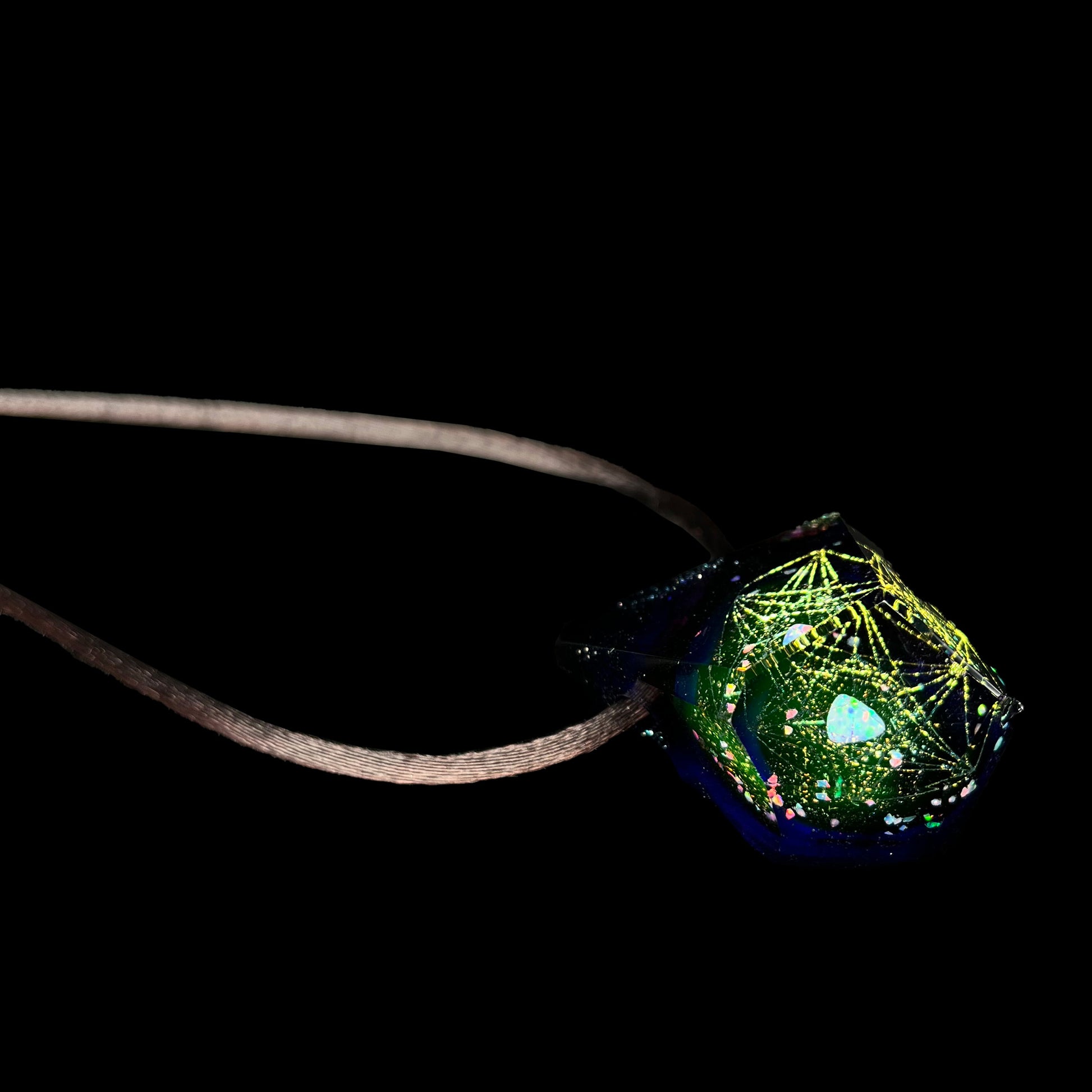 A purple faceted glass and lab-created opal necklace on a brown cord, shown from an angle laying on a black background.