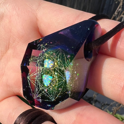 Hand holding a crystal-shaped glass pendant with a lab-created opal inside, faceted by artist, Josh Arleth.