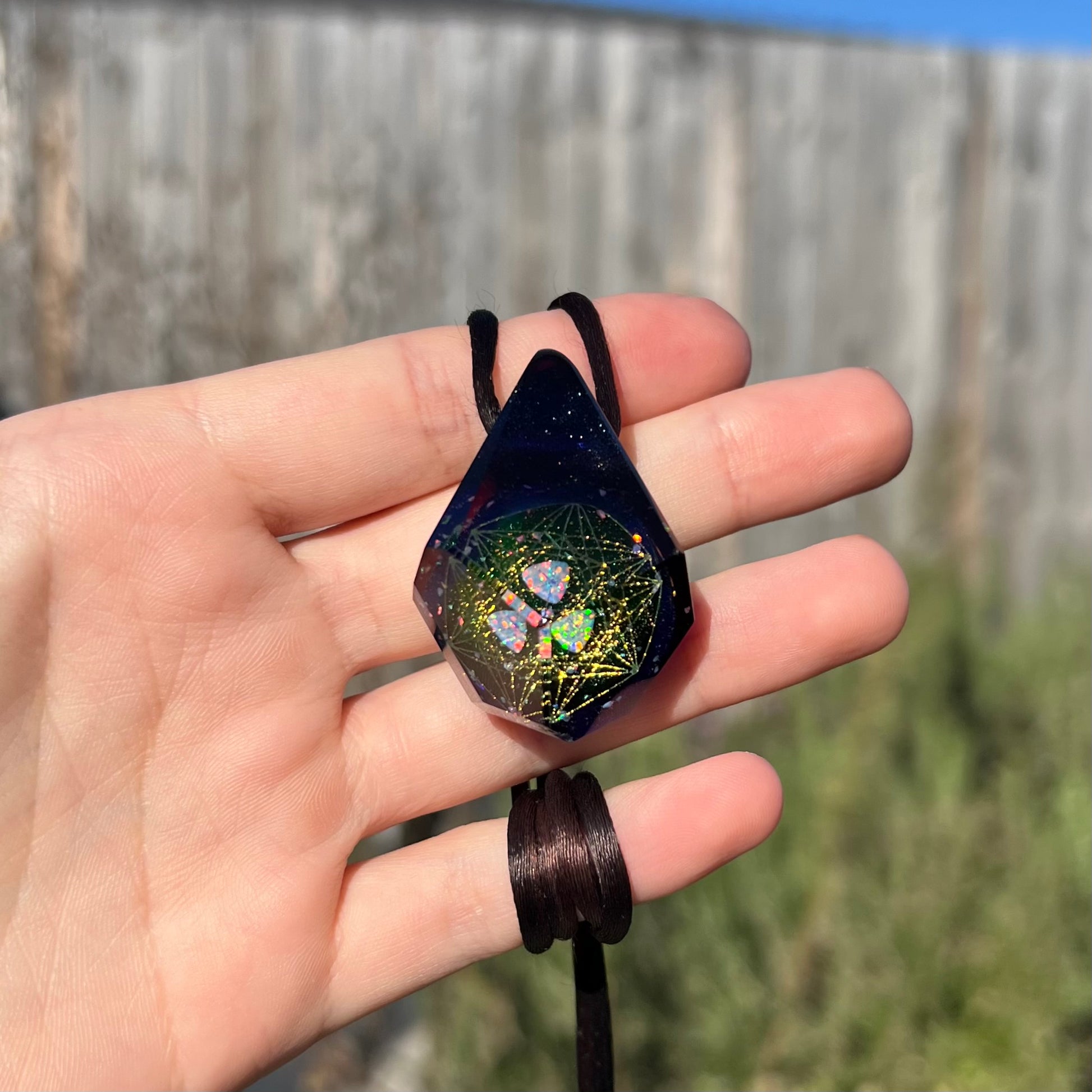 Hand holding a purple faceted glass necklace featuring a trillion cut lab-created opal that reflects across multiple facets, shown in the sunlight.