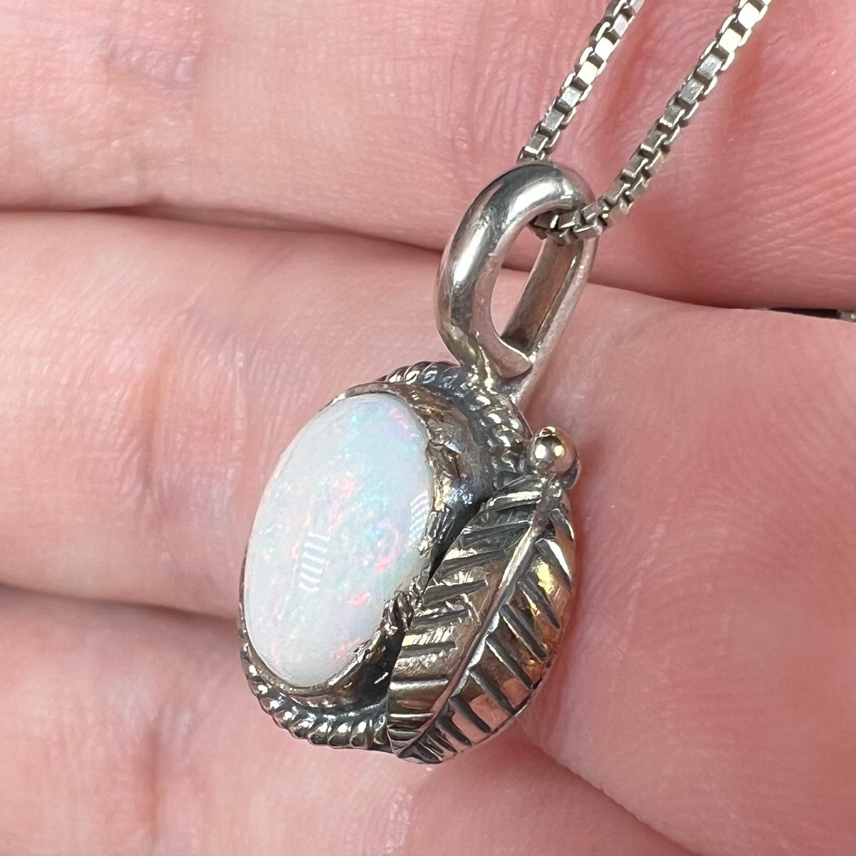 Close-up of feather design opal solitaire pendant in sterling silver, held in hand