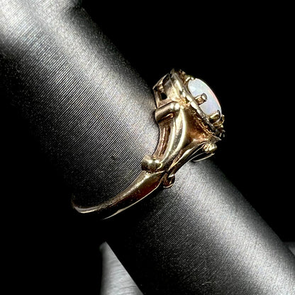 A ladies' Art Nouveau style opal solitaire ring.  The mounting is yellow gold with filigree accents.