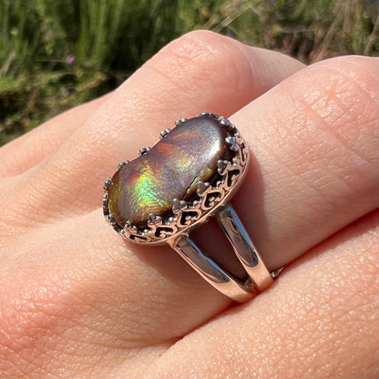 A fire agate ring with a crown design worn on finger at an angle in sunlight, highlighting a crack in the stone.