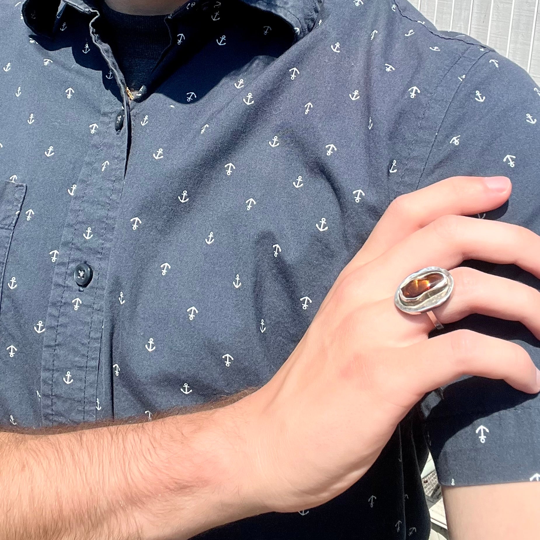 A handmade sterling silver fire agate ring worn on a model's hand as the hand rests on the model's opposing shoulder.