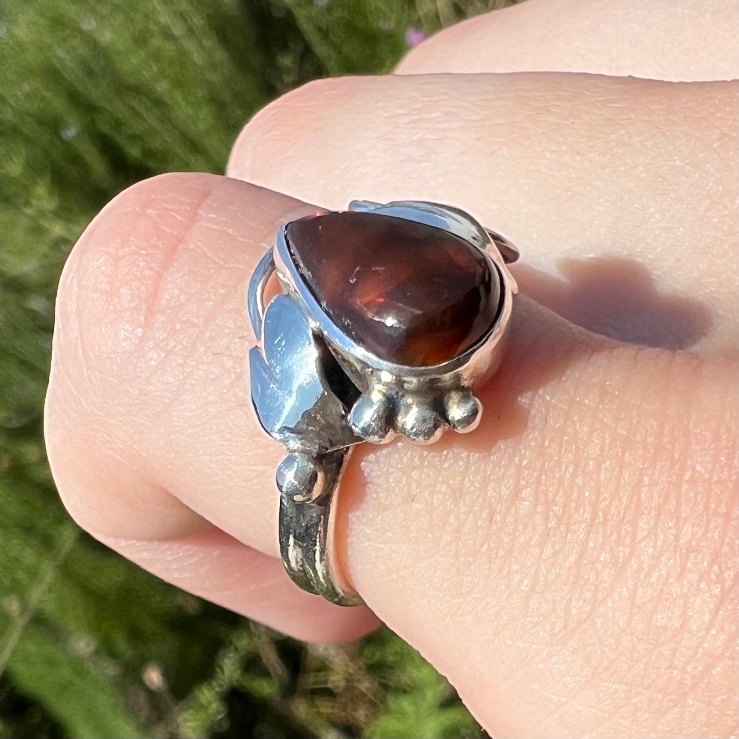 Angled close-up of a ladies' pear shaped fire agate ring with a sterling silver leaf design worn in the sun.