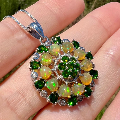 A fire opal and chrome diopside necklace, held at an angle in the sunlight.