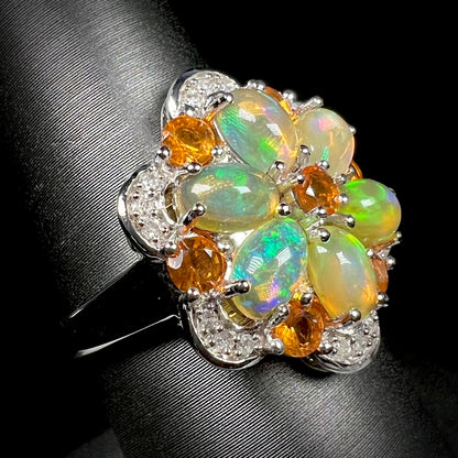 A fire opal and diamond cluster ring that resembles a flower, shown at an angle against a black background.
