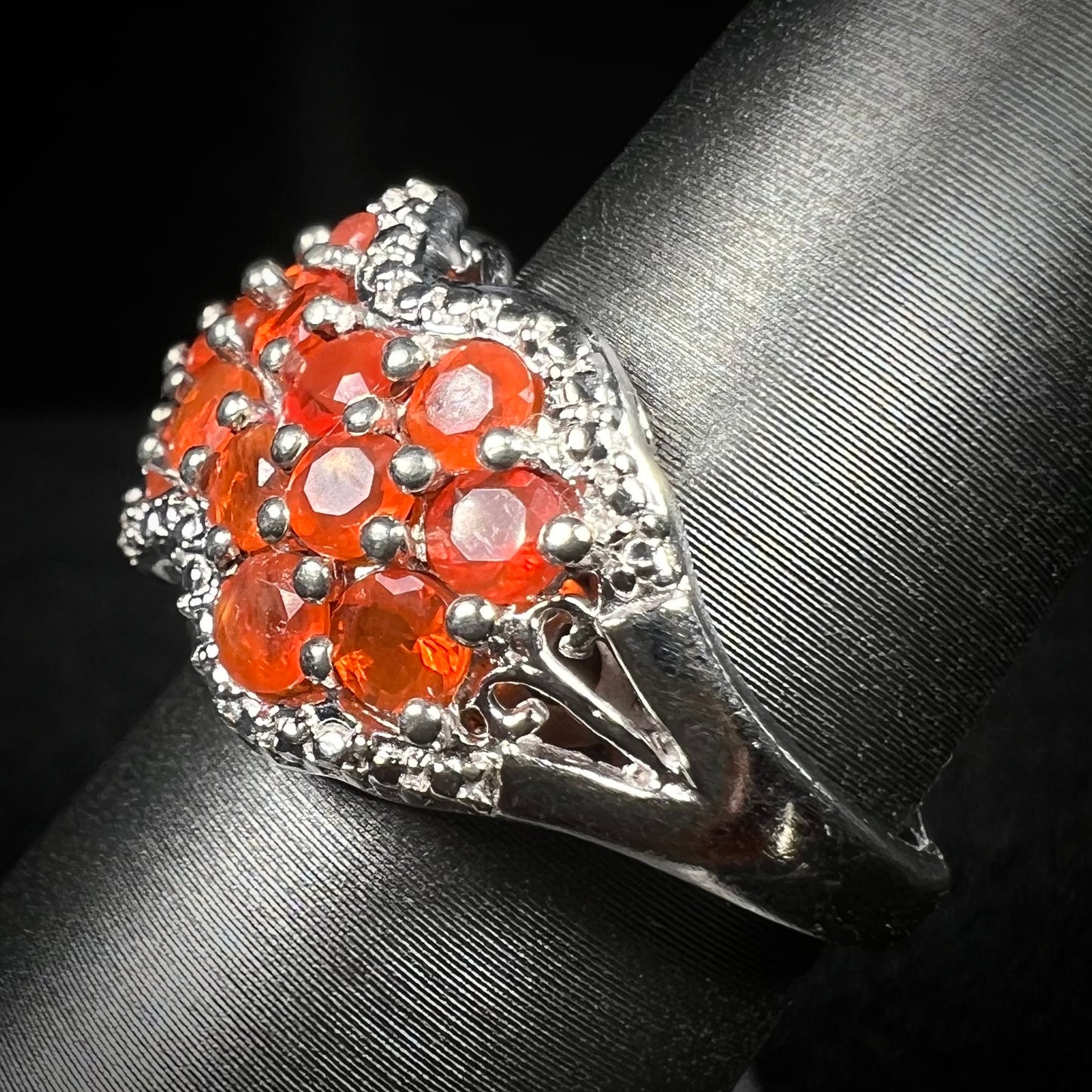 Side close-up view of a Mexican fire opal cluster ring on a ring display; a filigree accent in the ring's shank is in focus.