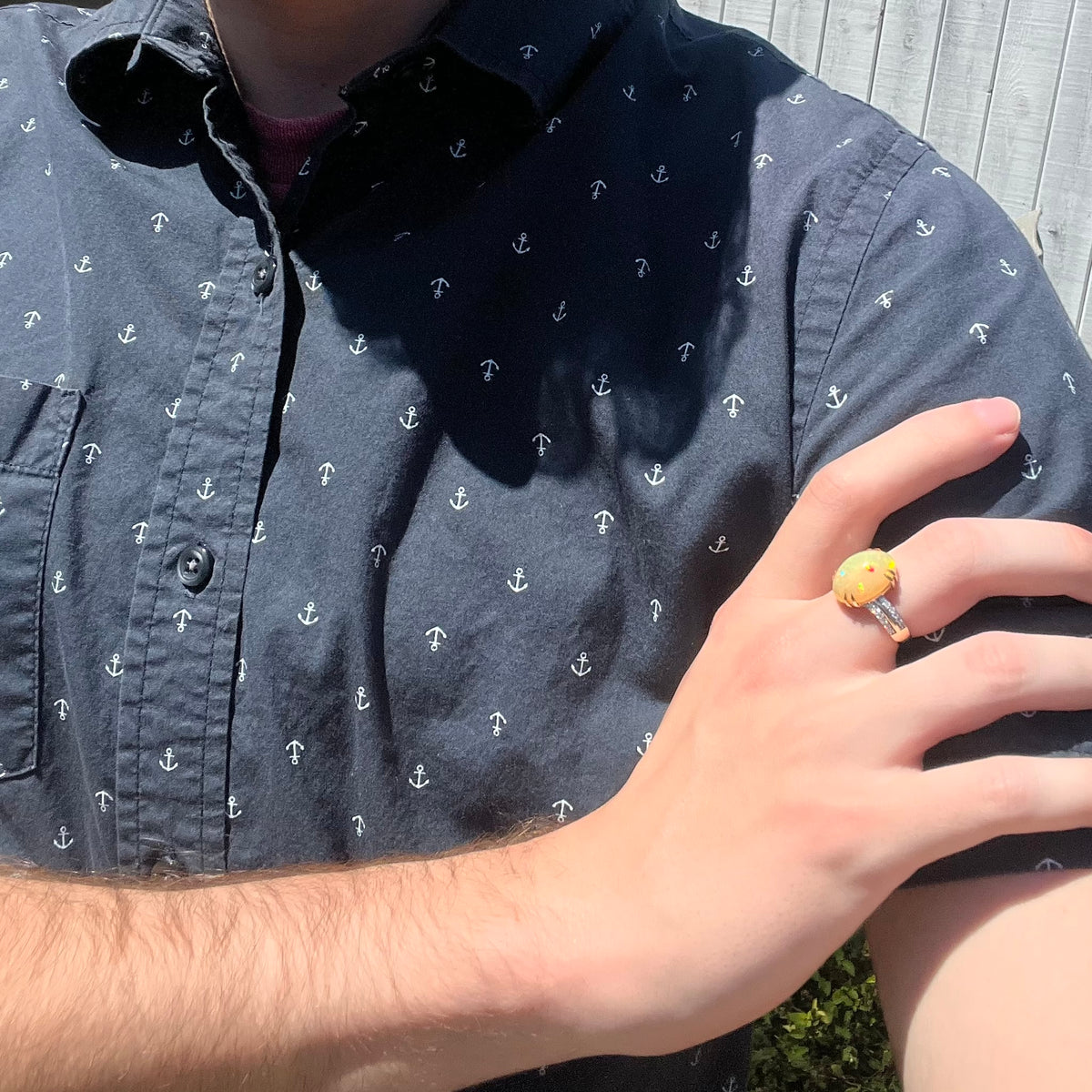 Close-up of person resting hand on opposing shoulder in sunlight wearing a fire opal and diamond women's cocktail ring