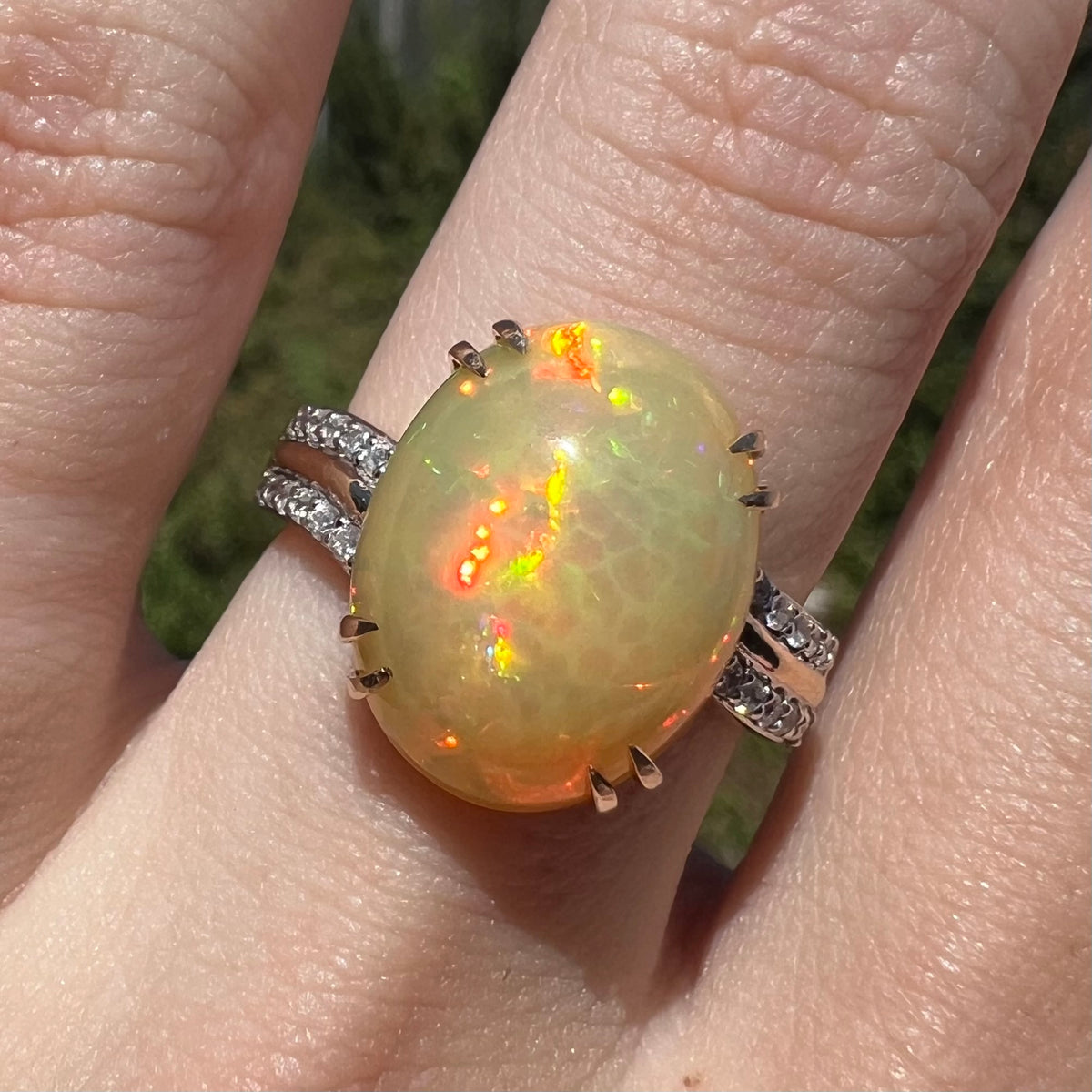 Close-up of Ethiopian fire opal and diamond ring, worn on finger in sunlight.  Opal has red and orange flashes
