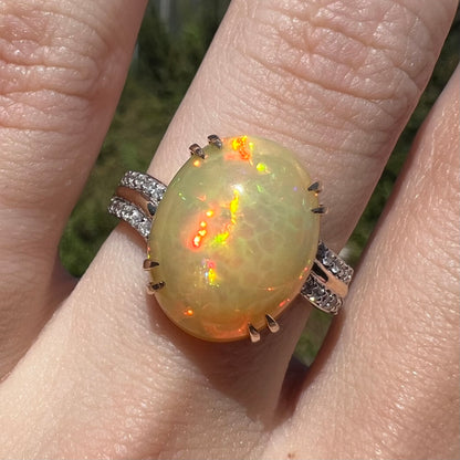 Close-up of Ethiopian fire opal and diamond ring, worn on finger in sunlight.  Opal has red and orange flashes