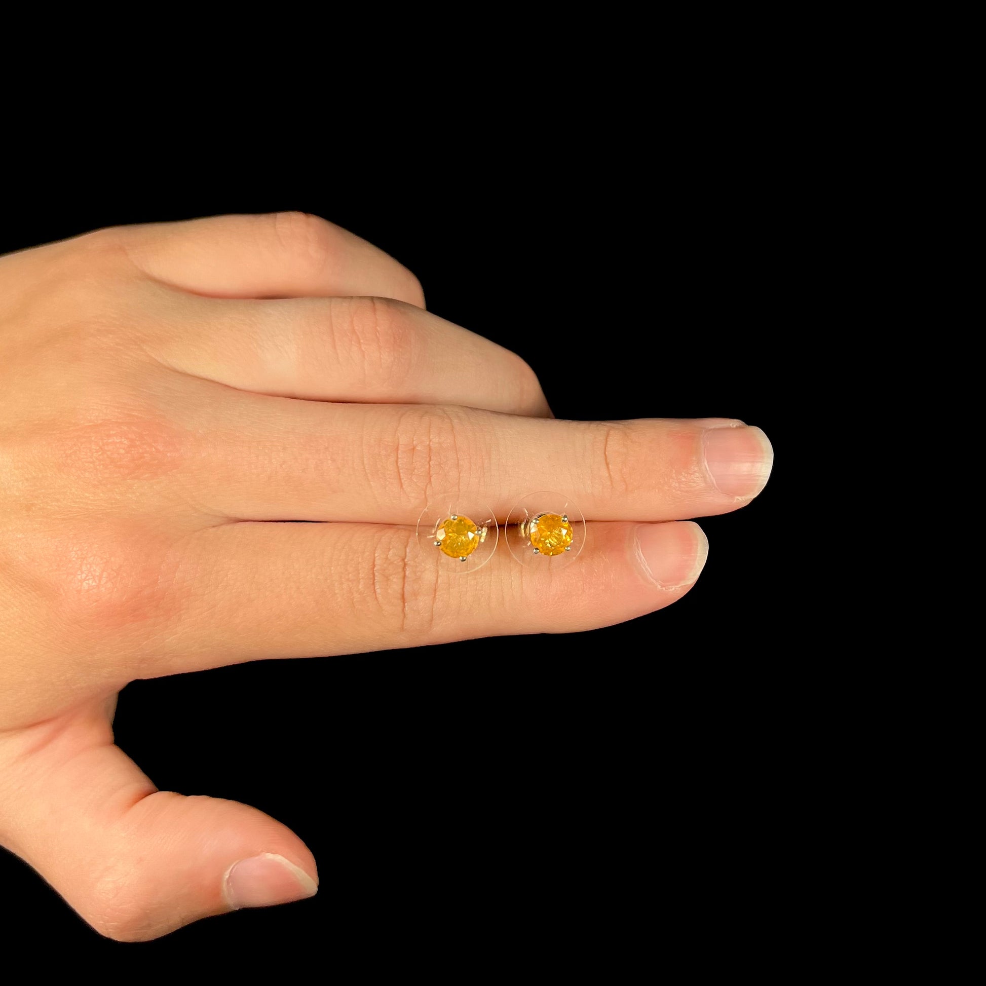 A pair of Mexican fire opal stud earrings in sterling silver, held between two fingers of a hand.