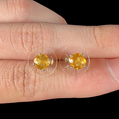 Close-up of Mexican fire opal stud earrings in sterling silver, held between two fingers.
