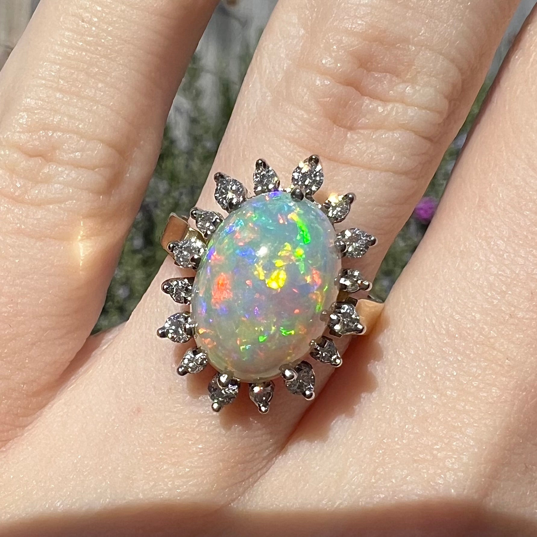 A macro close-up of a 4.30ct Lightning Ridge fire opal engagement ring worn on the engagement finger in sunlight.  The opal's fire appears brilliant and multicolored.