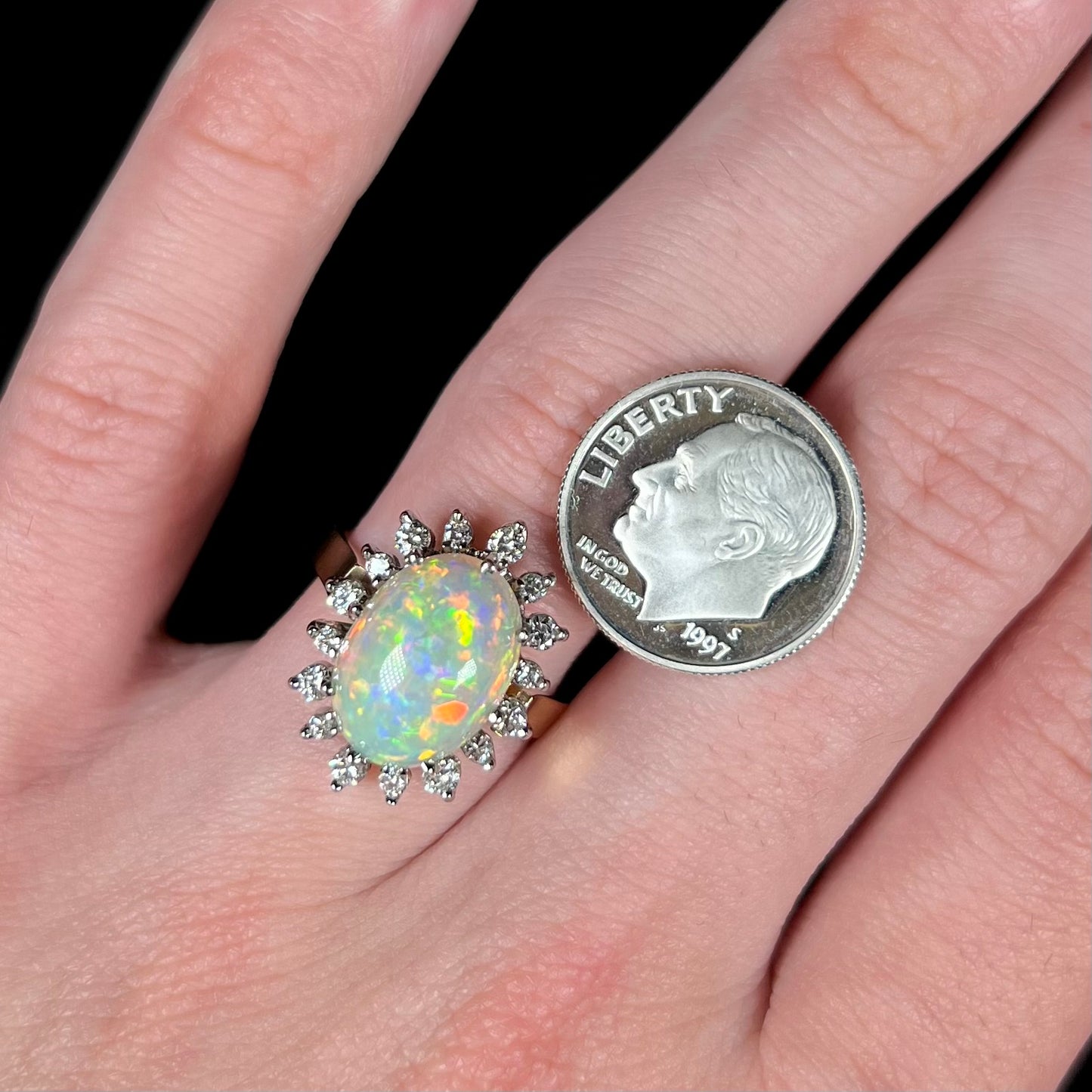 A 4.30ct Lightning Ridge fire opal engagement ring worn on a hand against a black background.  A dime coin is placed next to the ring for scale.