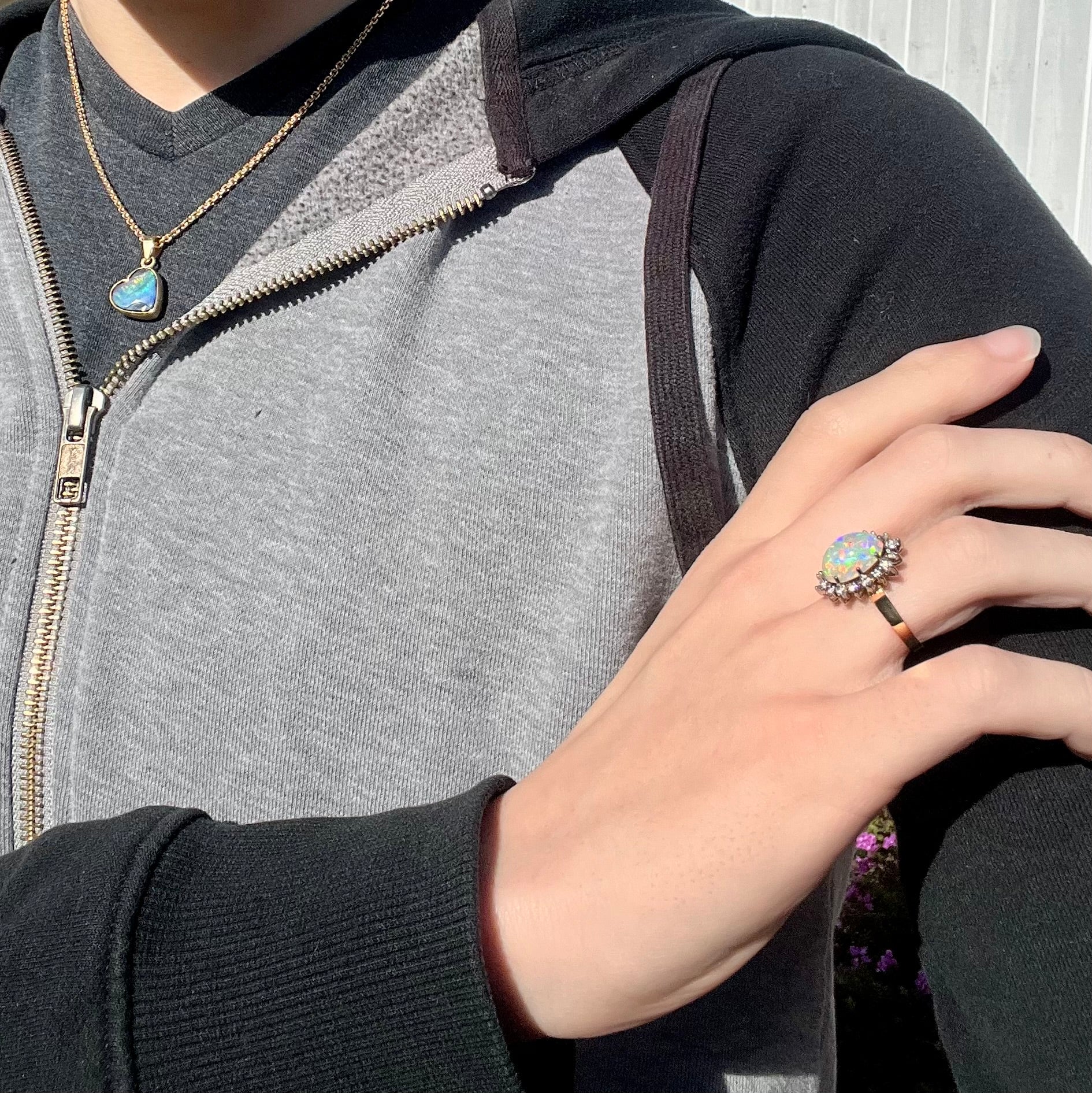 A lifestyle shot of a 4.30ct Lightning Ridge fire opal engagement ring worn on a hand resting on the opposite shoulder.  The opal displays multicolored fire in sunlight.