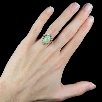 A 4.30ct Lightning Ridge fire opal engagement ring worn on the engagement finger.  The hand is set against a black background, showcasing the ring's design.