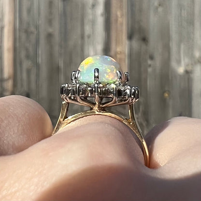 A profile view of a 4.30ct Lightning Ridge fire opal engagement ring worn on the engagement finger in the sunlight.  The white gold diamond halo is highlighted.