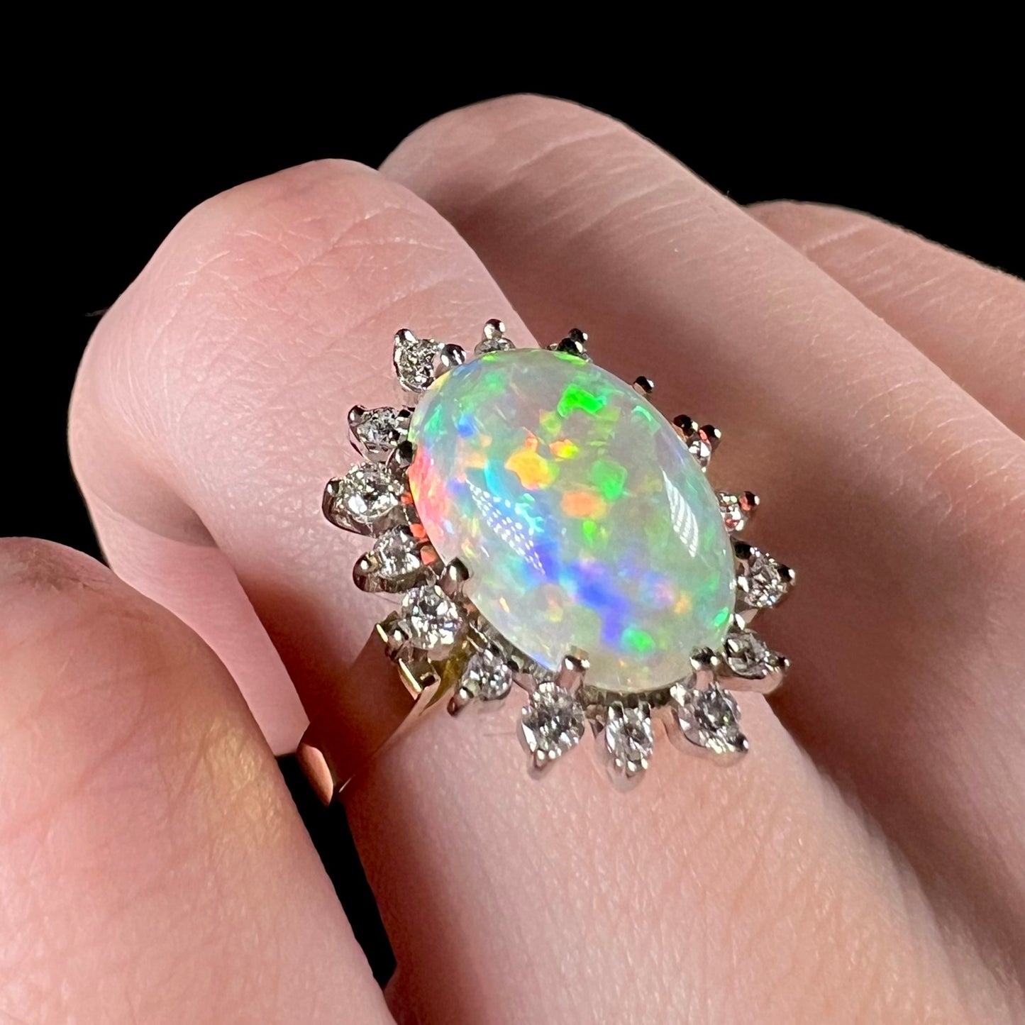 A close-up of a 4.30ct Lightning Ridge fire opal engagement ring worn on the engagement finger.  The opal displays a purple ribbon effect with green and red flashes.