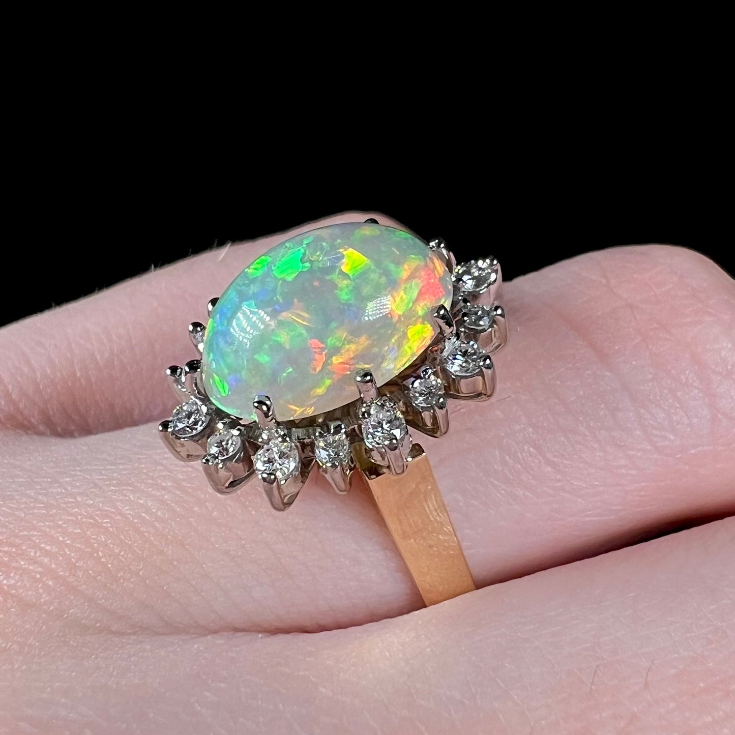 A close-up view of a 4.30ct Lightning Ridge fire opal engagement ring worn on the engagement finger.  The opal displays intense green, yellow, and red fire.