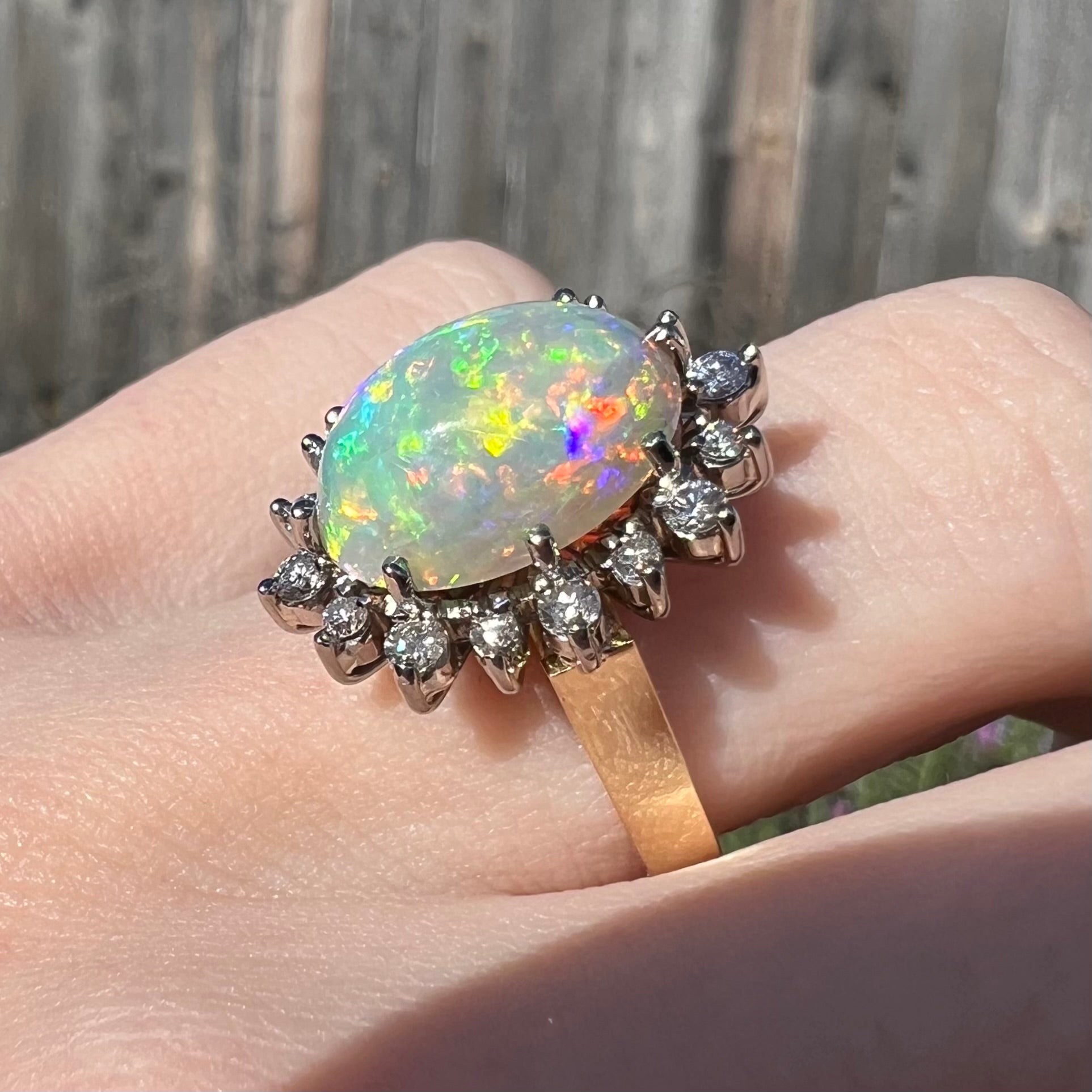 A close-up of a 4.30ct Lightning Ridge fire opal engagement ring worn on the engagement finger in sunlight.  The opal's fire is predominantly yellow with multicolor flashes.