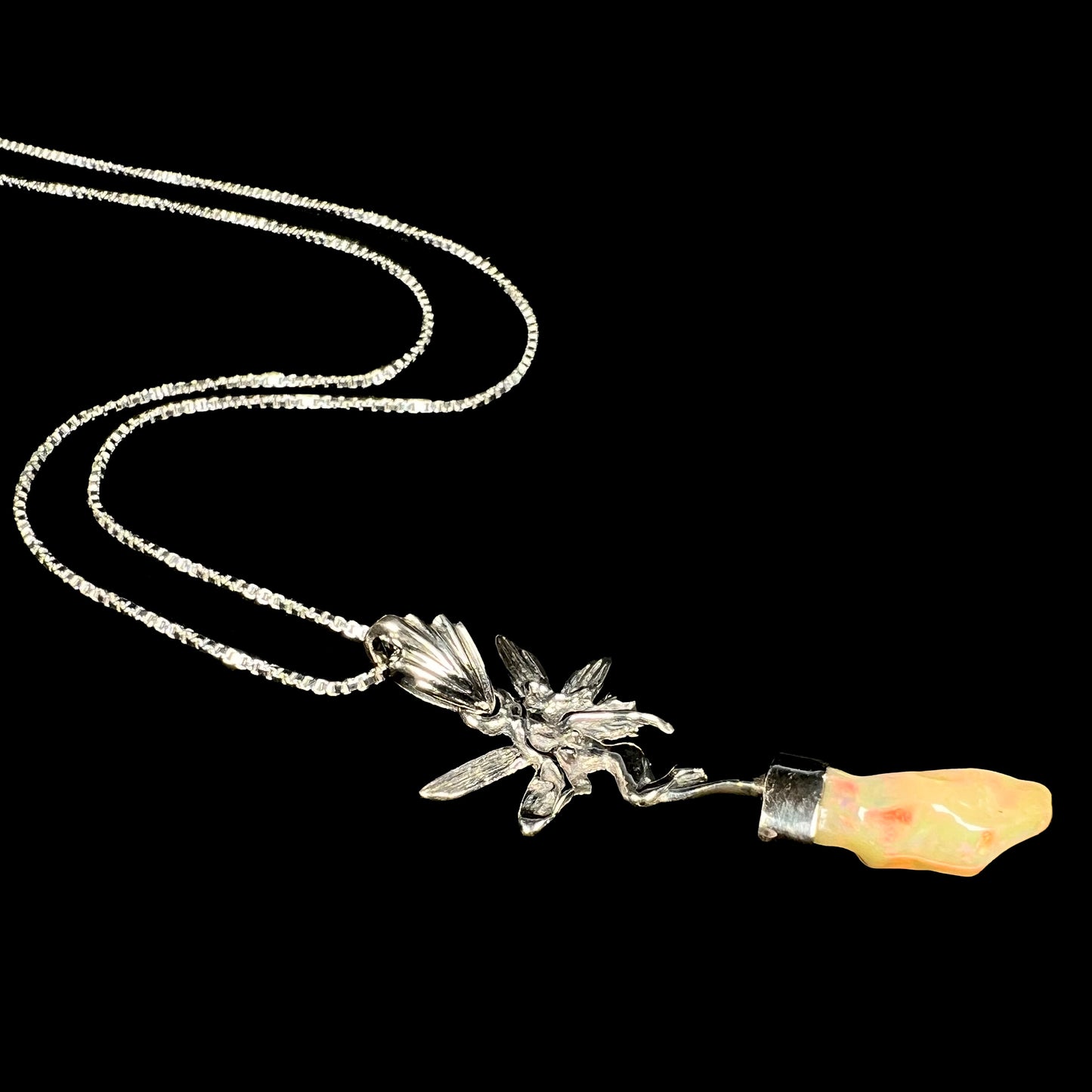 A sterling silver fairy necklace with an Ethiopian fire opal crystal, shown from an angle laying against a black background.