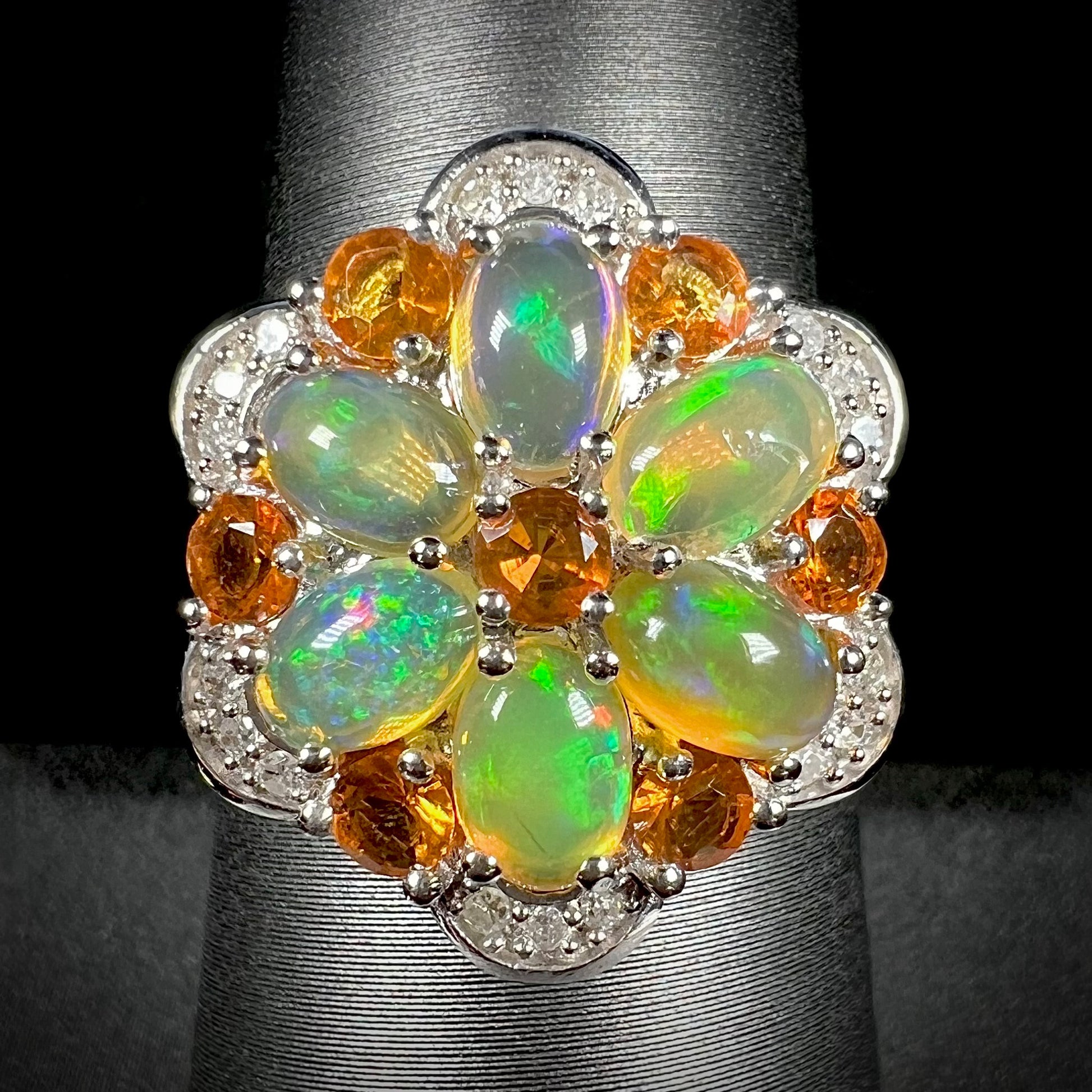 Front close-up of silver fire opal and diamond flower ring against a black background.