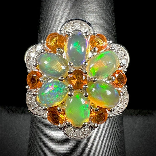 Front close-up of silver fire opal and diamond flower ring against a black background.