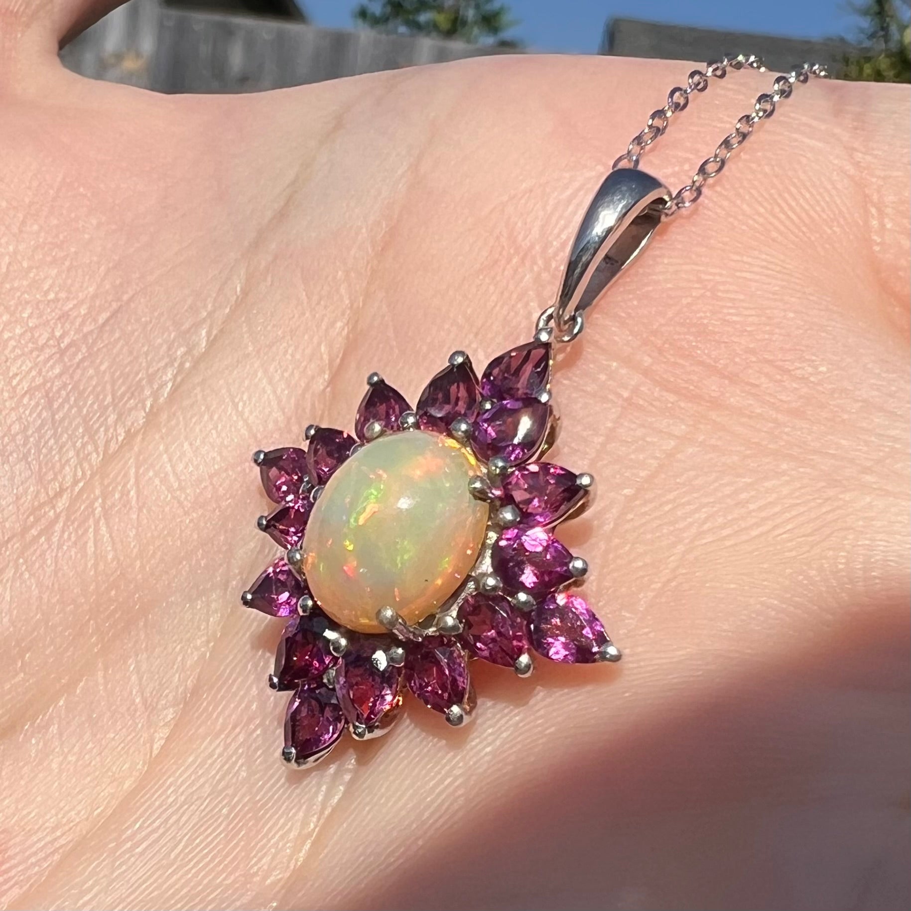 Sunlit angled close-up of a sterling silver Ethiopian opal and rhodolite garnet spray necklace.