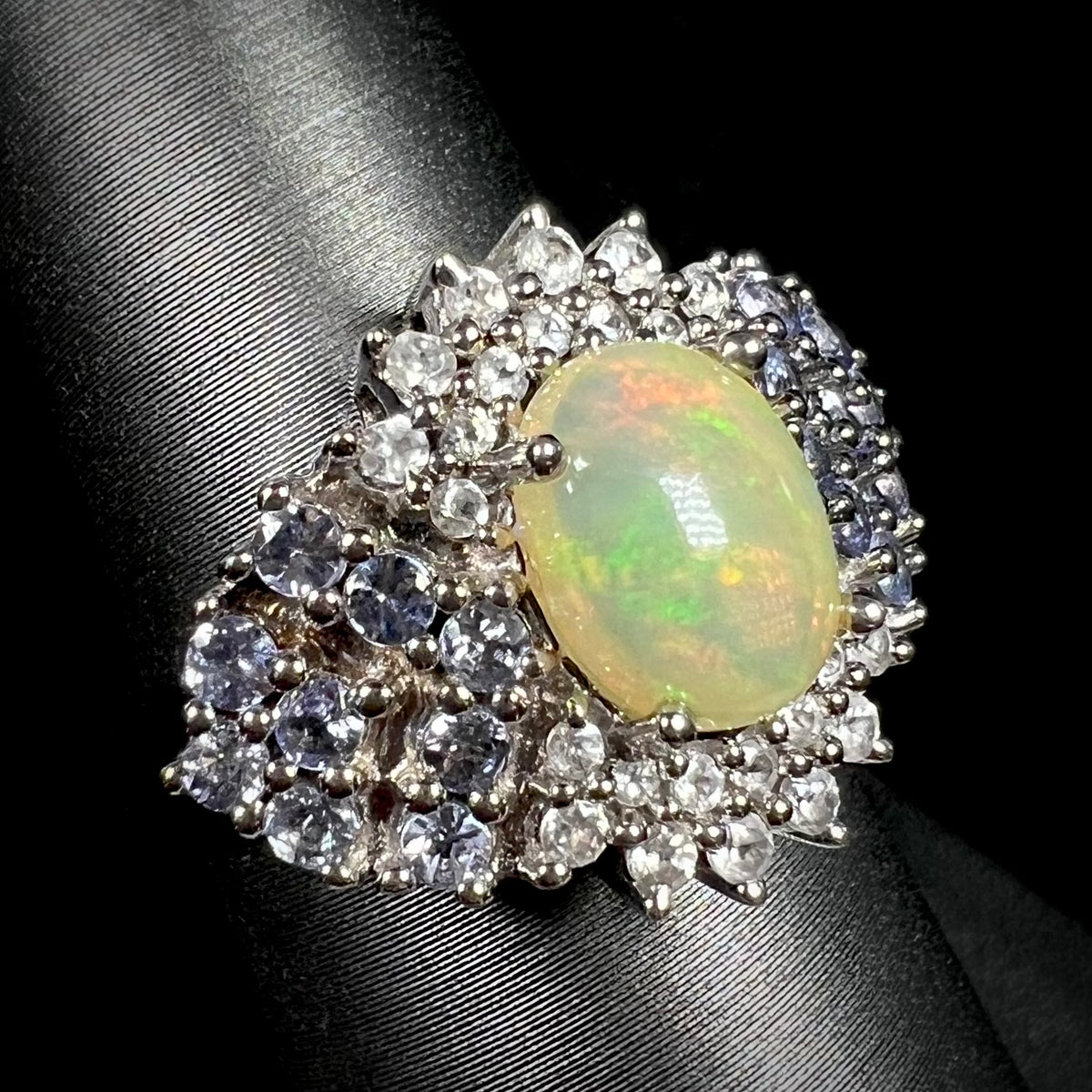 Ethiopian fire opal ring with cluster of blue and white gemstone accents, shown on ring display