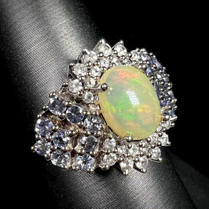 Ethiopian fire opal ring with cluster of blue and white gemstone accents, shown on ring display
