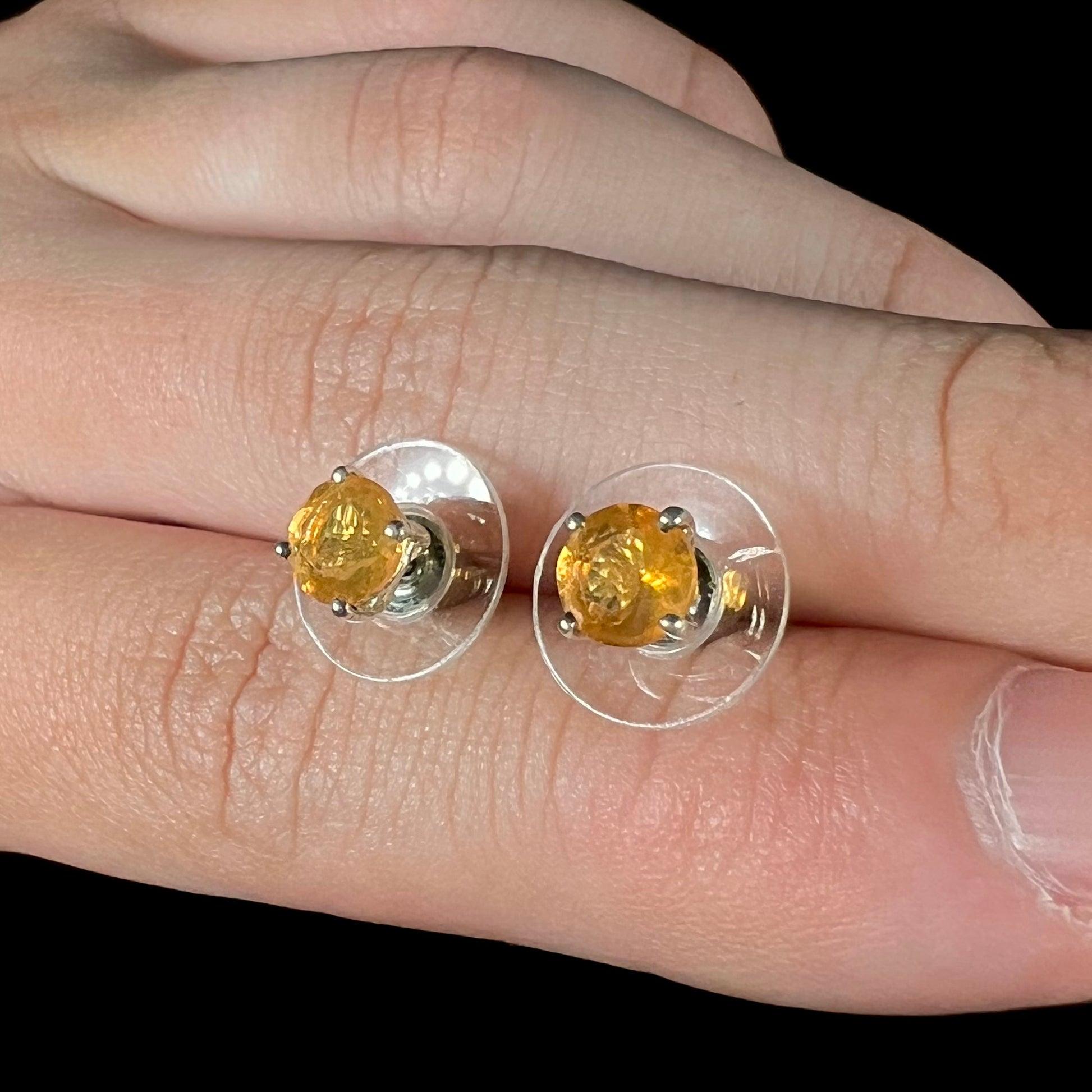 A pair of Mexican fire opal stud earrings in sterling silver held between two fingers at an angle.
