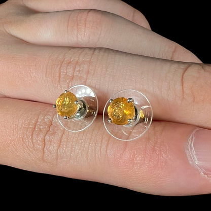 A pair of Mexican fire opal stud earrings in sterling silver held between two fingers at an angle.