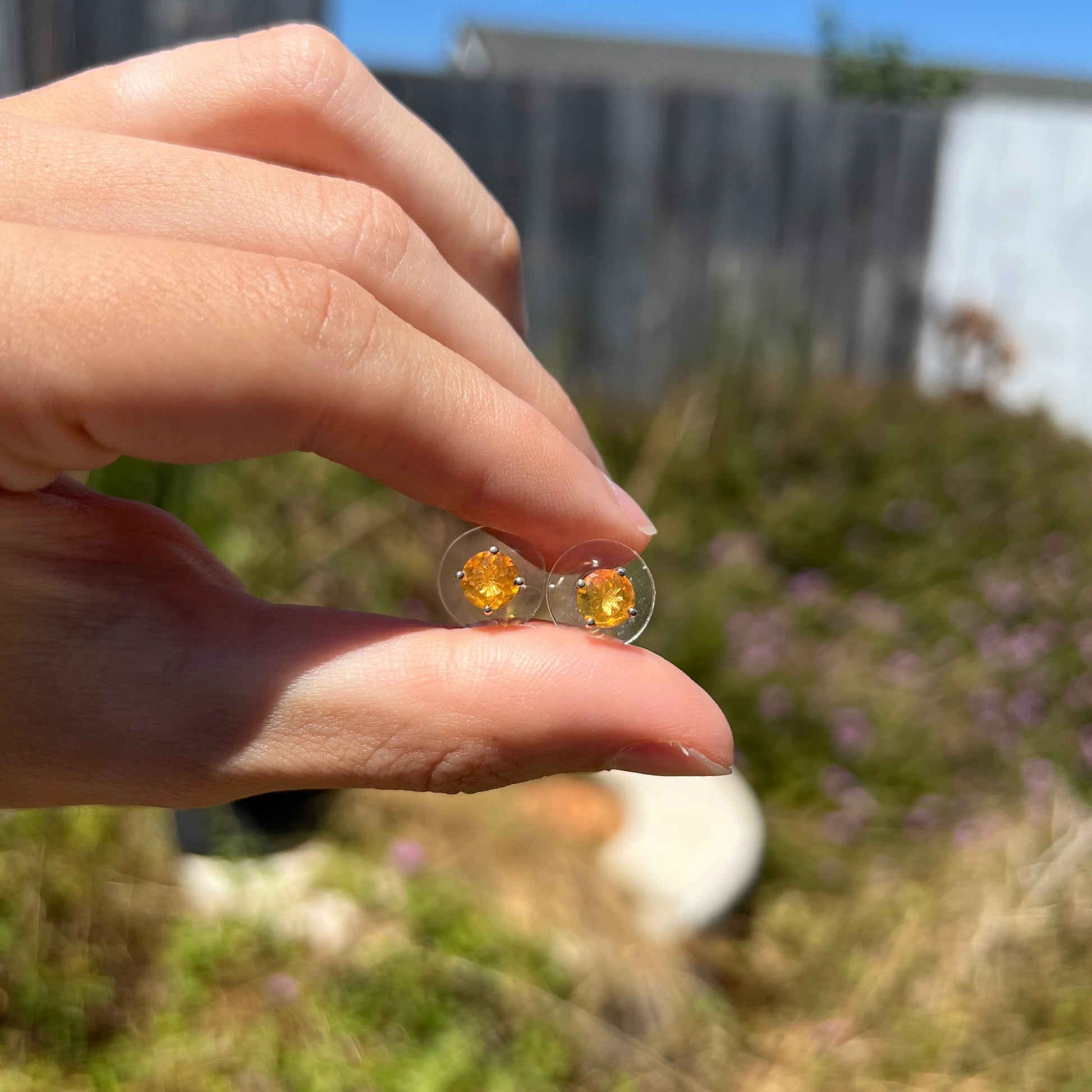 A pair of Mexican fire opal stud earrings in sterling silver shown at a distance in daylight.